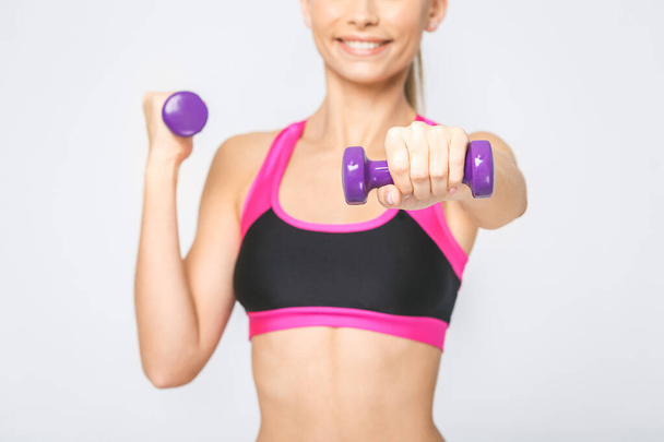 Close-uo de feliz joven fitness mujer levantando pesas sonriente y enérgico. Aislado sobre fondo blanco
. - Foto, imagen
