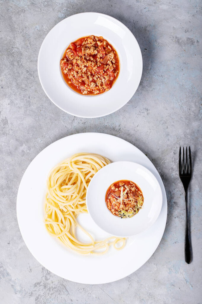 Cooked spaghetti bolognese served with black pepper and saslt in white ceramic plate over white texture background. Top view, flat lay. Copy space - Фото, изображение
