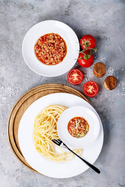 Cooked spaghetti bolognese served with black pepper and saslt in white ceramic plate over white texture background. Top view, flat lay. Copy space - Photo, Image