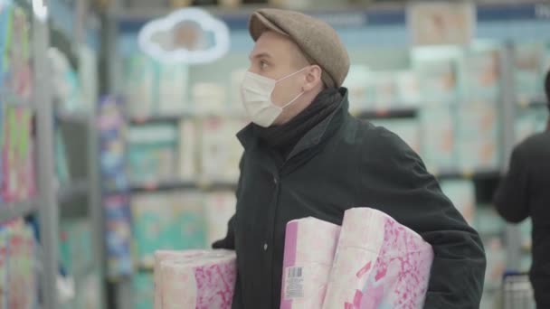 Man in mask and protective gloves buying toilet paper in shop. Panic at coronavirus epidemic - Footage, Video