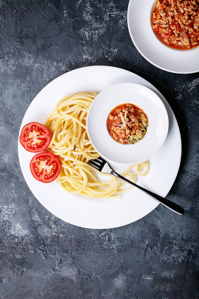Cooked spaghetti bolognese served with black pepper and saslt in white ceramic plate over dark texture background. Top view, flat lay. Copy space - Fotó, kép