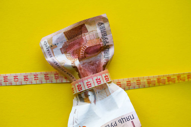 Close up of money being squeezed by measuring tape on top of coins.Close-up view of russian rubles banknote with measuring tape on grey, financial crisis concept - Fotoğraf, Görsel