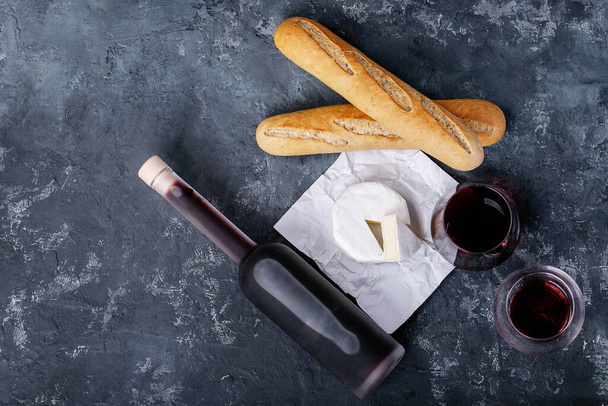 Szklanka czerwonego wina serwowana z serem camembert i francuską bagietką na ciemnym tle tekstury. Widok z góry, płaski. Przestrzeń kopiowania - Zdjęcie, obraz