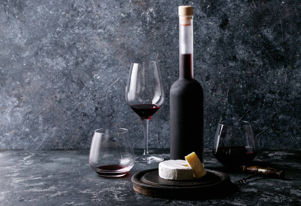 Glass of red wine served with cheese camembert, honey, jam and french baguette over dark texture background - Photo, image