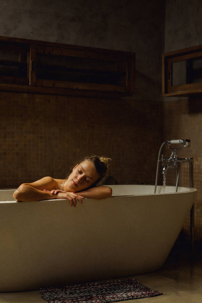 Hermosa mujer caucásica sonriente posando con el pelo mojado en el baño, relajándose en el baño en el baño. mujer joven acostada en la bañera
. - Foto, imagen