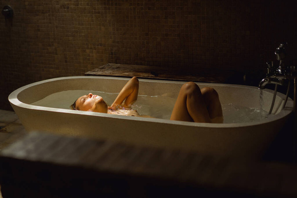 Beautiful smiling Caucasian woman posing with wet hair at bathroom, relaxing in the bath in the bathroom. young woman lying in bathtub. - Фото, зображення