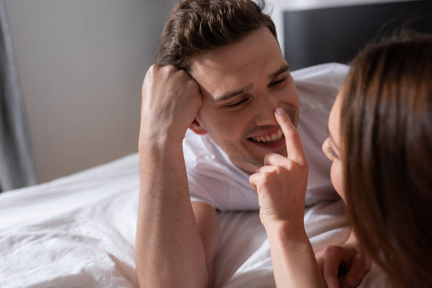 selective focus of cheerful girl touching nose of happy boyfriend in bedroom  - Fotografie, Obrázek