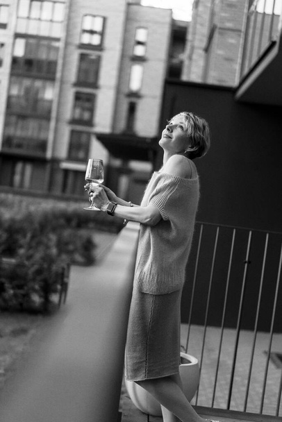 Beautiful woman on the terrace with a glass of wine is resting, laughing. black and white photo. - Foto, Imagen