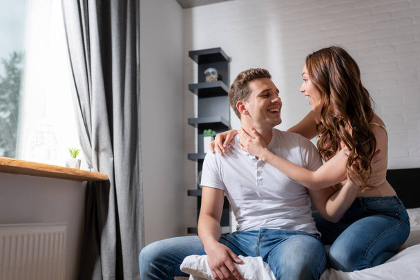cheerful couple looking at each other and smiling in bedroom  - Photo, Image