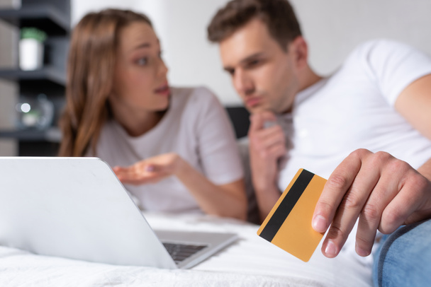 вибіркова увага задумливого чоловіка, який тримає кредитну картку поруч з дівчиною і ноутбуком.  - Фото, зображення