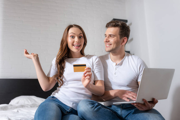 glückliche Frau mit Kreditkarte neben fröhlichem Mann und Laptop  - Foto, Bild