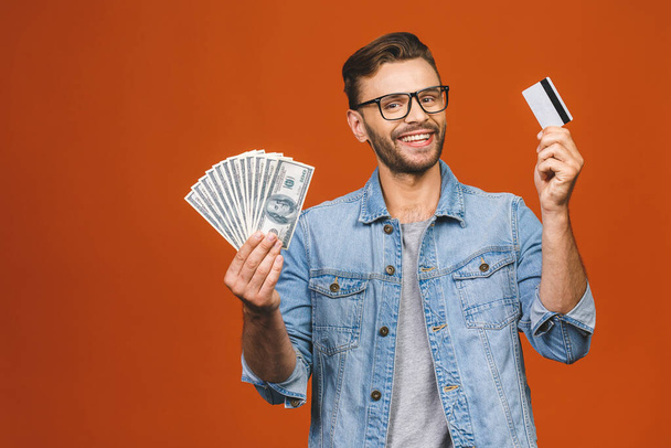 Image of shocked excited young handsome bearded man posing isolated over orange wall background holding money and credit card make winner gesture. - Photo, Image