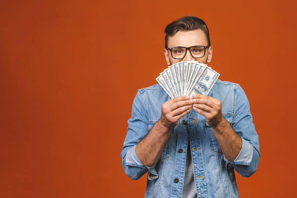Image of shocked excited young handsome bearded man posing isolated over orange wall background holding money make winner gesture. - Foto, immagini