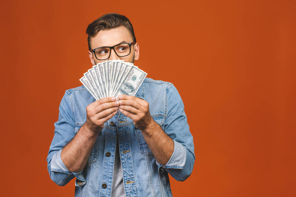 Image of shocked excited young handsome bearded man posing isolated over orange wall background holding money make winner gesture. - Foto, Bild
