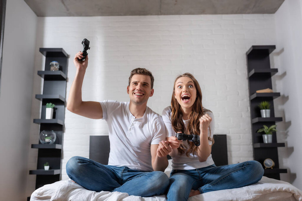 KYIV, UKRAINE - MAY 15, 2020: excited woman and happy man playing video game in bedroom  - Фото, зображення