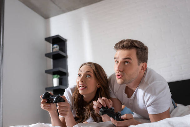KYIV, UKRAINE - MAY 15, 2020: excited woman and emotional man playing video game in bedroom  - Foto, Imagen