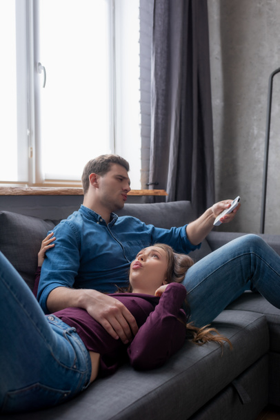 displeased woman lying near boyfriend holding remote controller from air conditioner while feeling hot  - Fotografie, Obrázek