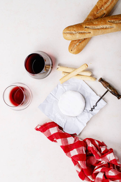 Glass of red wine served with cheese camembert and french baguette over white texture background. Top view, flat lay. Copy space - Фото, изображение