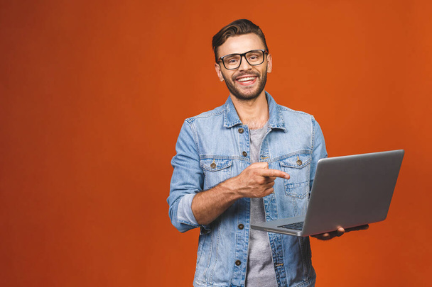 Indoor portrait of young man in casual standing against orange backgroundl with copy space for ads, holding laptop, smiling.  - Foto, Imagen