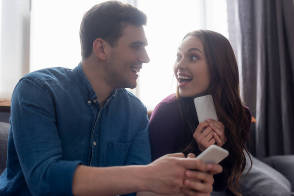 Selektiver Fokus des fröhlichen Paares, das sich anschaut und Smartphones in der Hand hält  - Foto, Bild