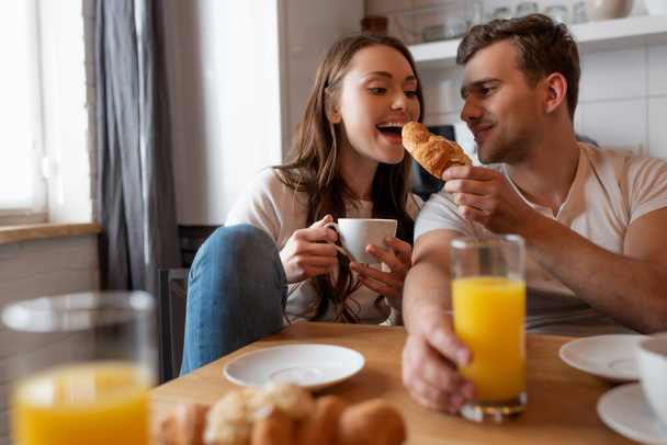 selective focus of happy man feeding cheerful girl with tasty croissant  - Fotoğraf, Görsel