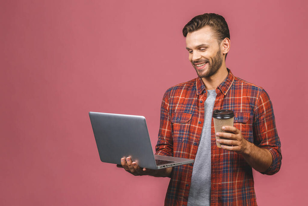 Retrato de hombre joven en posición informal sobre fondo rosa con espacio de copia para anuncios, sosteniendo el ordenador portátil con sonrisa feliz. Beber café o té
.  - Foto, imagen