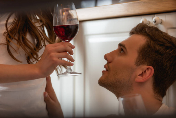 γυναίκα που κρατάει ένα ποτήρι κόκκινο κρασί κοντά σε έναν όμορφο άντρα  - Φωτογραφία, εικόνα