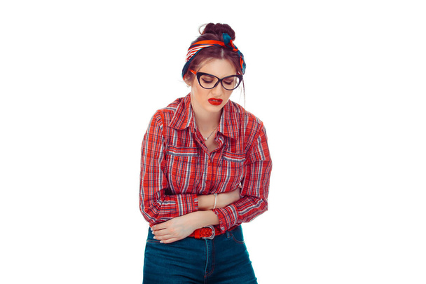 Young woman holding her stomach. She is having a menstruation pain. Closeup portrait of a beautiful mixed race girl in red checkered shirt and jeans with retro bow on head isolated on white background - Fotoğraf, Görsel