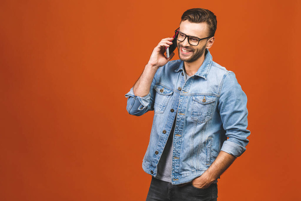 Glücklich lächelnder junger Mann spricht auf Handy isoliert auf orangefarbenem Hintergrund. - Foto, Bild