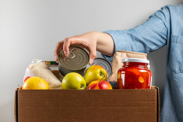 Female hand puts tin can in food donation box - Фото, зображення