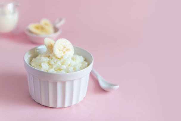 Milk rice porridge with banana in a white mask on a pink background, can be used for article, banner and infographic - Fotografie, Obrázek