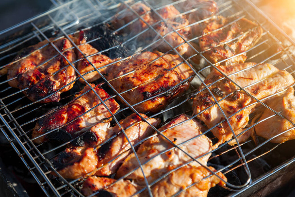Assorted meat in a grill for barbecue frying illuminated by fire from firewood close-up with burnt edges. Outdoor dinner for the company at the cottage. - Photo, Image