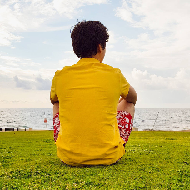 Un joven se sienta en la orilla del mar y mira a la distancia. Se sienta de espaldas al espectador. Plaza foto, estilo de vida
. - Foto, imagen