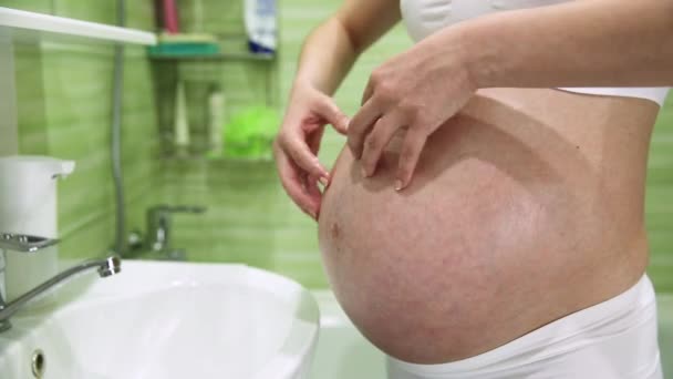 těhotná dívka poškrábe žaludek se smetanou pro strie v koupelně - Záběry, video