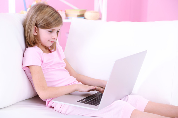 Bambina seduta con computer portatile sul divano in camera
 - Foto, immagini