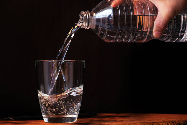 het gieten van gezuiverd fris drinkwater uit de fles op houten aanrecht en ruimte voor tekst - Foto, afbeelding