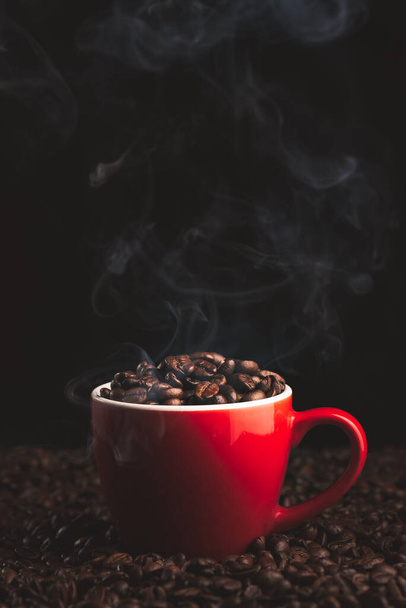 Červený pohár s kouřením a kouřící kávová zrna na stole pokryté kávovými zrny.Káva tematické pozadí - Fotografie, Obrázek