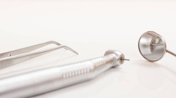 High-speed dental handpiece, metal mirror and tweezers. Dental instruments for dental treatment on black background. Medical tools. Close-up view. Shallow depth of field. Focus on a metal mirror. - Photo, Image