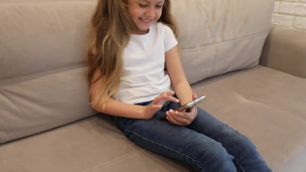 Casual baby sitting on a couch at home playing and touching a mobile phone - Filmati, video