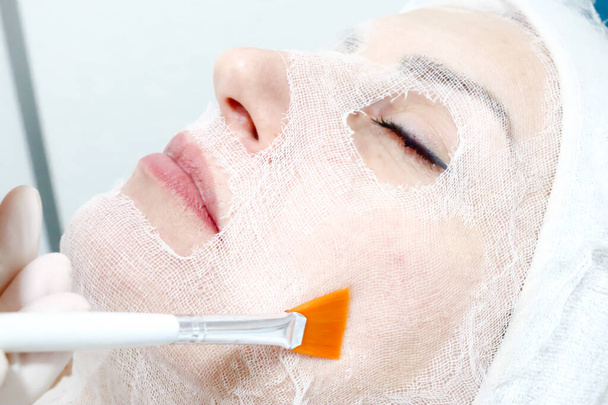 Kosmetikerin mit Pinsel bei der biologischen Behandlung einer Kundin im Schönheitssalon, Augen geschlossen, Gesicht mit Gaze bedeckt, Nahaufnahme  - Foto, Bild