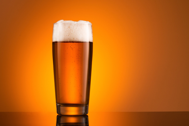 Glass of beer with foam on orange background - Foto, Imagem