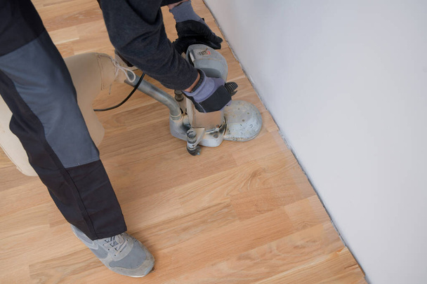 Scraping floor surface with grinding machine. Repair in the apartment. Carpenter grinder parquet in a narrow corner with a small machine - Photo, Image