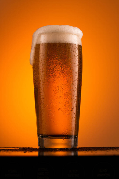 Vidro de cerveja com espuma em fundo laranja - Foto, Imagem