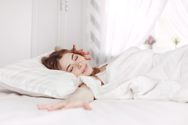 Schattig slaperig meisje strekt zich uit op het bed om wakker te worden in de vroege ochtend. Lichte achtergrond, ruimte voor tekst - Foto, afbeelding