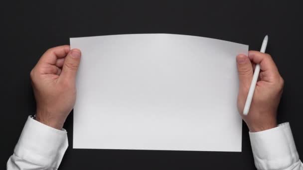 top view of a blank sheet of paper and a businessman's hands on a black table, white shirt and wrist watch - Footage, Video