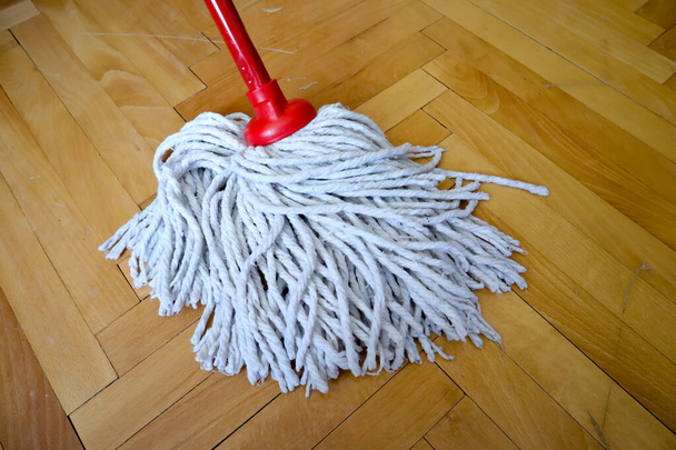 geïsoleerde reiniging dweil met rode houten stok op houten vloer, parket, reiniging en desinfectie van oppervlakken  - Foto, afbeelding