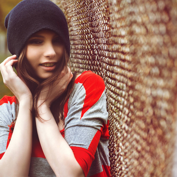 portrait of a beautiful girl in a hipster hat and striped jacket at the gate outdoor - Foto, afbeelding