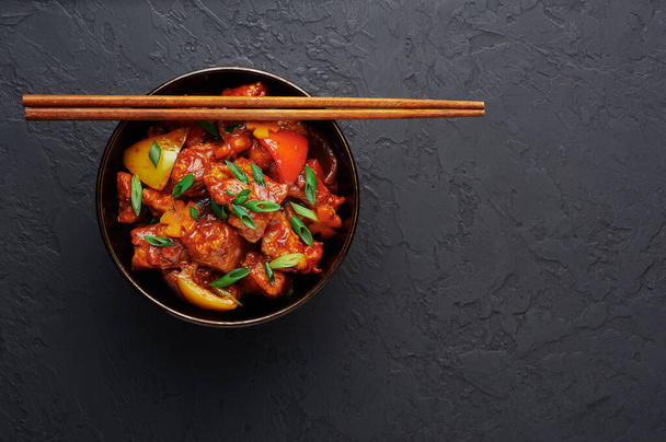 Chicken Manchurian in bowl at black concrete background. Chicken Manchurian is Indian Chinese cuisine dish with Chicken breasts, bell pepper, tomatoes, soy sauce. Copy space - Photo, Image