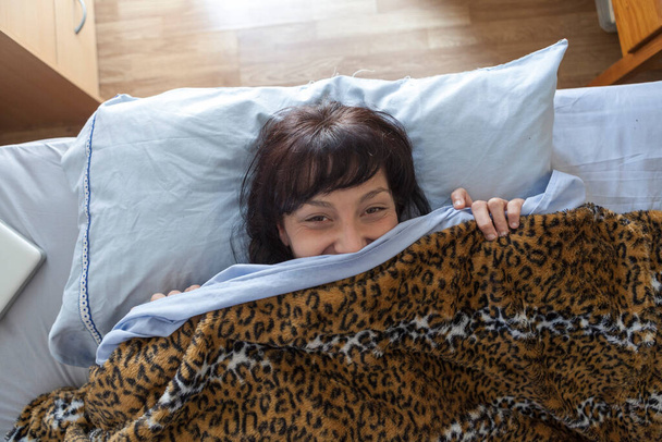 Eine junge Frau ist gerade aus einem Mittagsschlaf aufgewacht und hat ihr Handy benutzt. Luftaufnahme einer Frau, die mit passenden Leopardenbettchen und Handy im Bett liegt. Gerade erst aufgewacht. - Foto, Bild