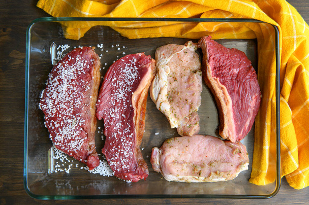 Hand seasoning a piece of raw meat with salt, preparing for a Brazilian barbecue. Flat lay. - Photo, Image